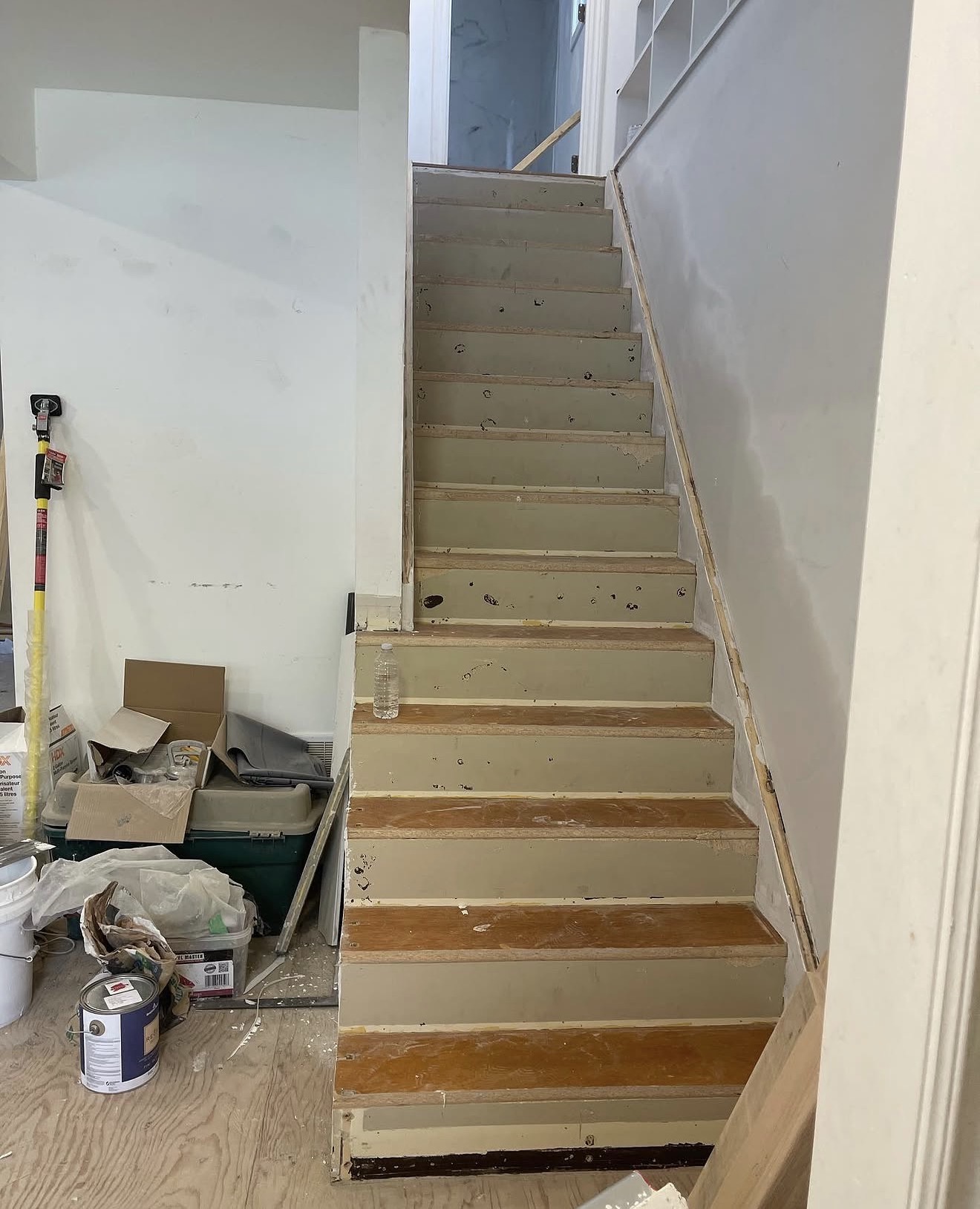 Staircase before renovation with bare treads, exposed plywood and unfinished drywall