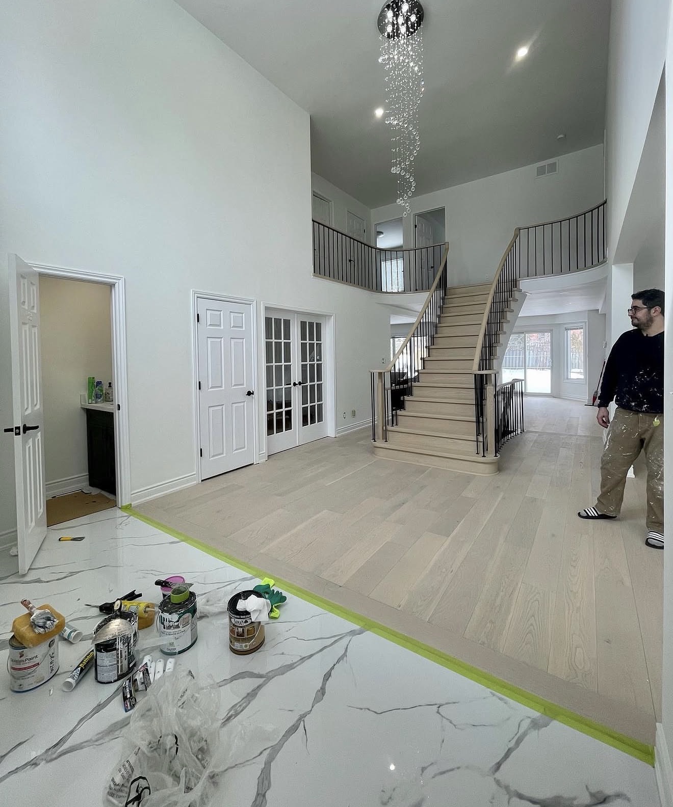 Two storey foyer with light hardwood floors, marble tile and a curved staircase mid-renovation